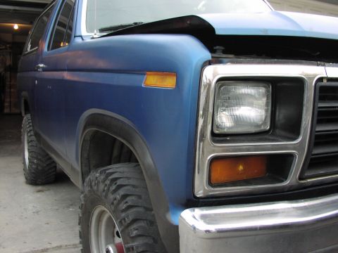1981 Ford Bronco - Close-up of a blue SUV's front corner, showing its grille and headlights.