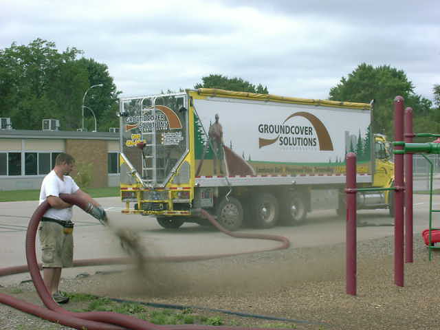 Man using hose connected to a truck labeled "GROUNDCOVER SOLUTIONS" to blow material