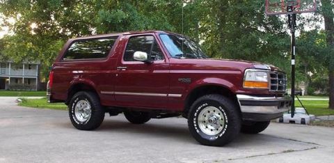 1996 Ford Bronco - A dark maroon/burgundy two-door Ford Bronco full-size SUV shown in a 3/4 front view, parked on a concrete driveway with trees and a basketb…