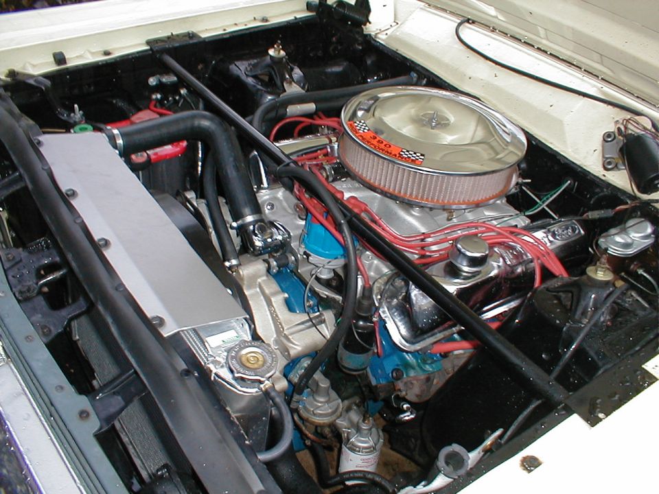 Engine bay of white Ford Fairlane with 390 V8, chrome air cleaner, red plug wires, aluminum radiator
