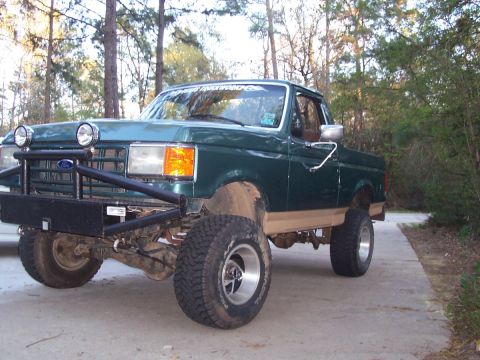 1989 Ford Bronco - This green Ford pickup truck, likely from the late 1980s, features a custom front bumper and raised suspension.
