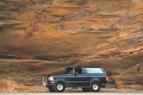 1993 Ford Bronco - 1993 Ford Bronco parked beside a cliff face ancient rock art.