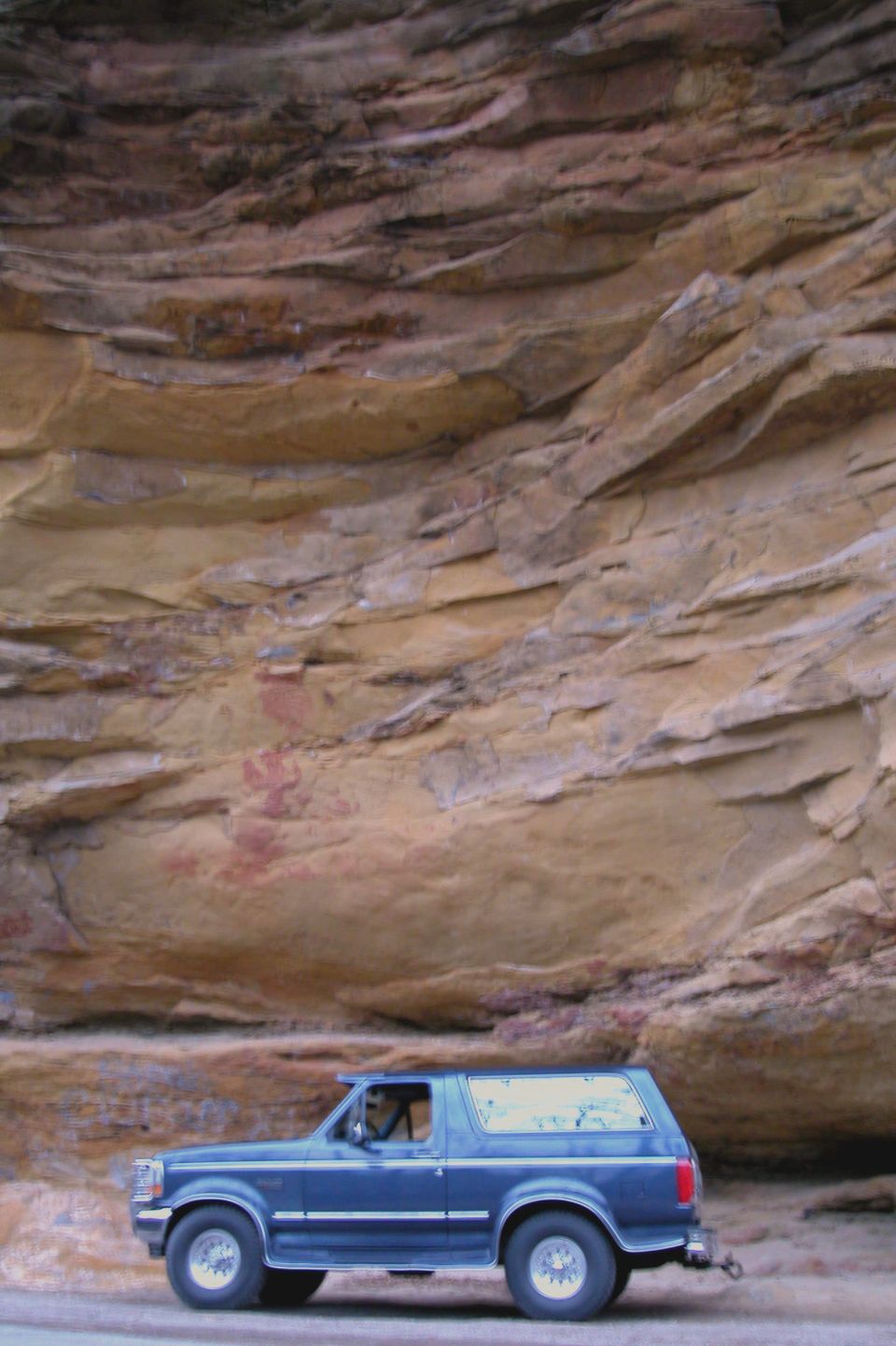 Blue 1993 Ford Bronco parked by a rock face with ancient paintings