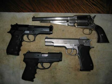 2002 Ford Taurus - Four handguns arranged on a cloth over a wood surface: a single-action percussion revolver, a black semi-automatic pistol, a compact black…