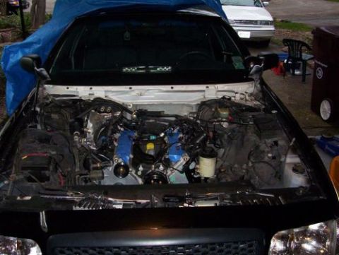 2000 Ford Crown Victoria - The engine bay of a car is exposed, with the engine removed and parts of the vehicle covered by a blue tarp.