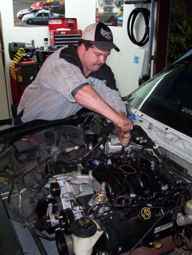 2000 Ford Crown Victoria - A mechanic works on the engine bay of a vehicle, with the Supermotors.net logo visible in the lower right corner.