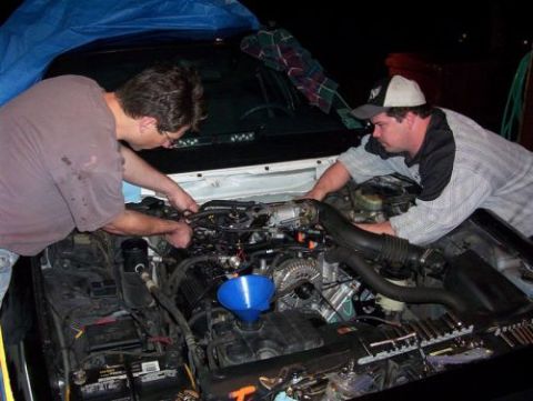 2000 Ford Crown Victoria - Mechanics are busy with engine work, with a blue funnel in place for fluid transfer.