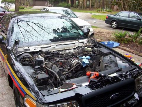 2000 Ford Crown Victoria - Engine bay of a 2000 Ford Crown Victoria with tools laid out for work. Multiple vehicles are visible in the background.