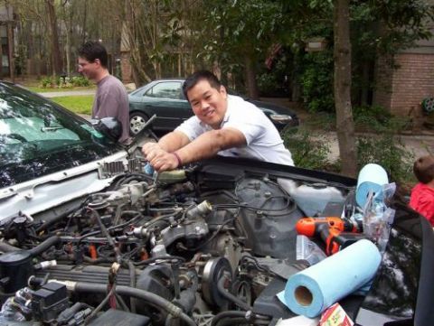 2000 Ford Crown Victoria - Two men work on the engine of a car, with another car visible in the background.
