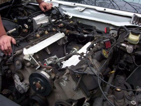 2000 Ford Crown Victoria - Hands are working on the engine bay of a vehicle, with various wires and parts visible.