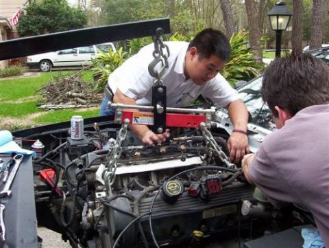 2000 Ford Crown Victoria - Mechanics use an engine hoist to remove a car's engine, with tools and a beverage can visible.