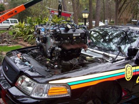 2000 Ford Crown Victoria - An engine is being lifted out of a black 2000 Ford Crown Victoria with the hood open.