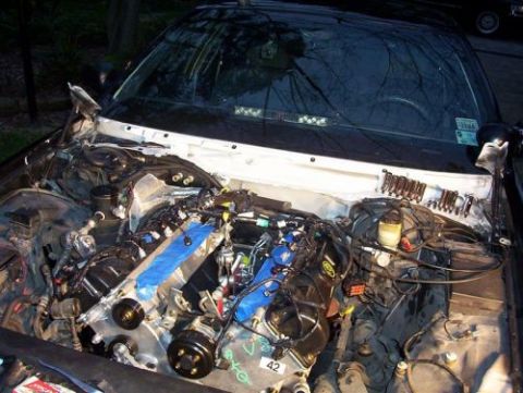 2000 Ford Crown Victoria - The engine bay of a vehicle is shown with the engine exposed and various wires and components visible. The SuperMotors.net logo is present…