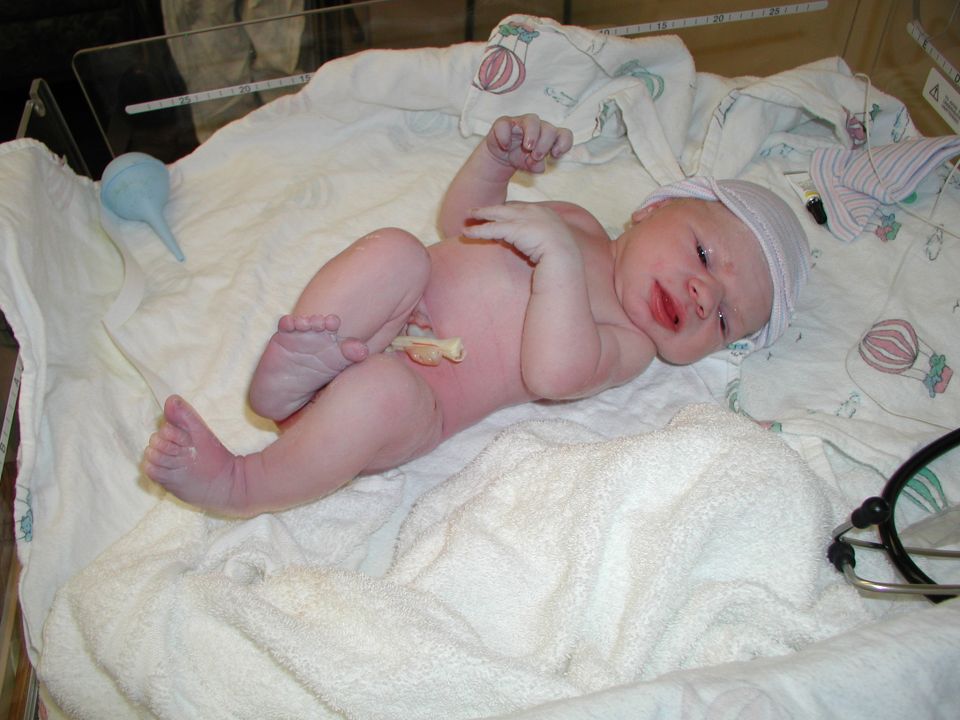newborn baby in a hospital bassinet with a blue bulb syringe and a stethoscope nearby