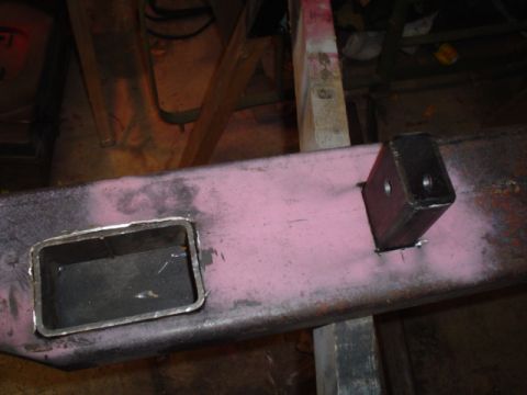 1981 Ford Bronco - Close-up of a fabricated square receiver tube welded through a pink-primered bumper or crossmember, with the trimmed opening ground flush o…
