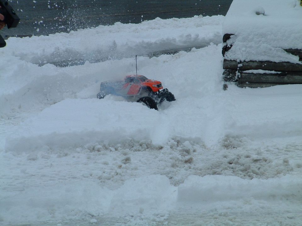 Orange remote-controlled monster truck driving through deep snow