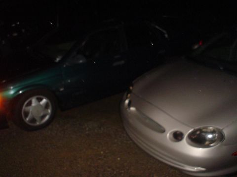1993 Ford Taurus - A silver 1996 Ford Taurus is parked next to a dark green car at night.