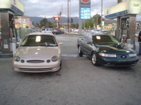 1993 Ford Taurus - Two Ford Taurus sedans are at a gas station. The green sedan appears to be a 1996 model.