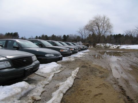 1991 Ford Crown Victoria LTD - Several dark sedans, including a 1991 Ford Crown Victoria LTD, are parked in a muddy lot with snow.