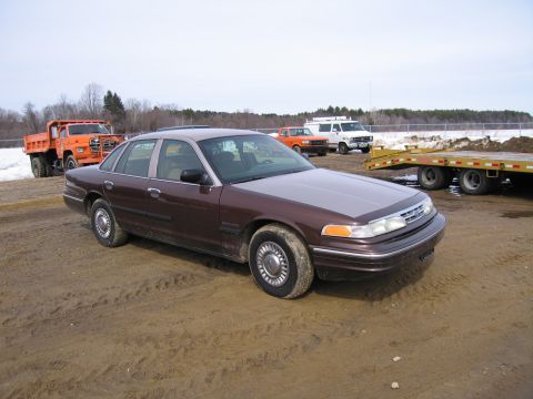 1991 Ford Crown Victoria LTD - A brown sedan is parked in a dirt lot with other vehicles and a trailer in the background.