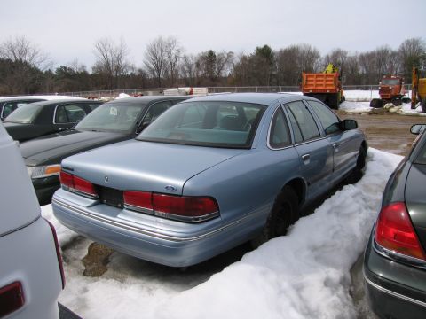 1991 Ford Crown Victoria LTD - Rear view of a 1991 Ford Crown Victoria LTD sedan in a snowy lot with other cars and construction equipment.