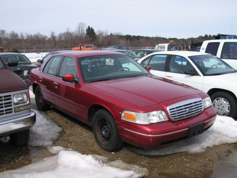 1991 Ford LTD Crown Victoria - Red aero-body Ford Crown Victoria four-door sedan on black steel wheels at a snowy surplus auction lot, front three-quarter view with a hol…