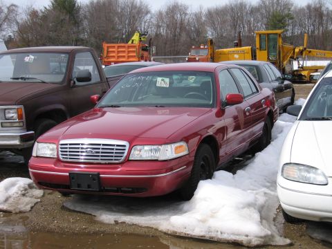 1991 Ford LTD Crown Victoria - Front three-quarter view of a dark red Ford Crown Victoria sedan at a municipal surplus auction, with "SURPLUS" and lot number 1676 grease-…