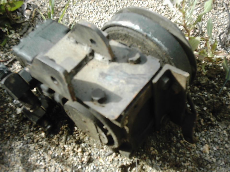 Close-up of a metal automotive brake caliper assembly resting on gravel