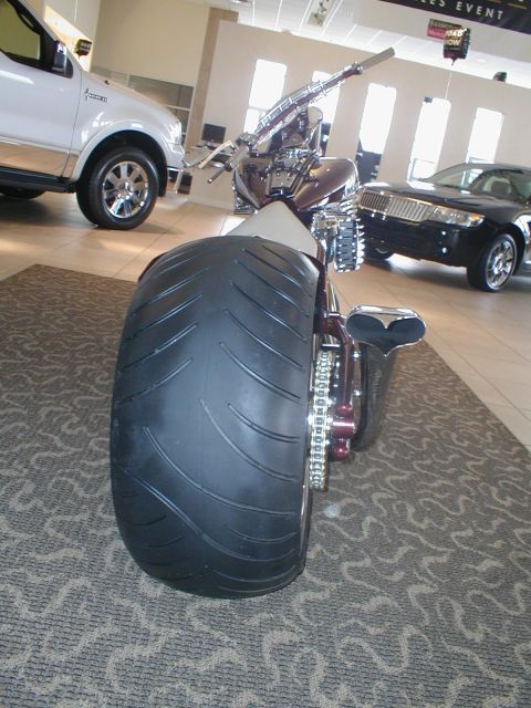 1979 Ford Bronco - A custom motorcycle with a massive rear tire is displayed indoors alongside other vehicles.