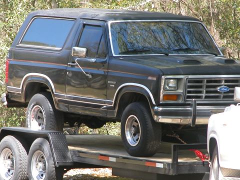 1986 Ford F-350 - A black Ford Bronco is loaded onto a trailer, viewed from the front three-quarter angle.