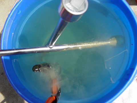 1988 Ford Bronco - A socket wrench and a metal part are submerged in a blue bucket of water, with visible text at the bottom.