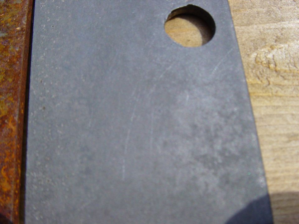 Rusted metal bracket with a circular hole drilled in it, resting on wood