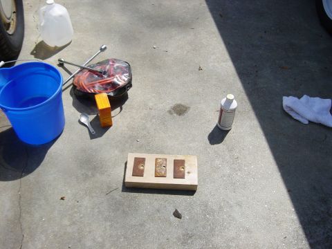 1988 Ford Bronco - Supplies for automotive repair are laid out on a concrete surface, including a bucket, water jug, and a block with metal plates.