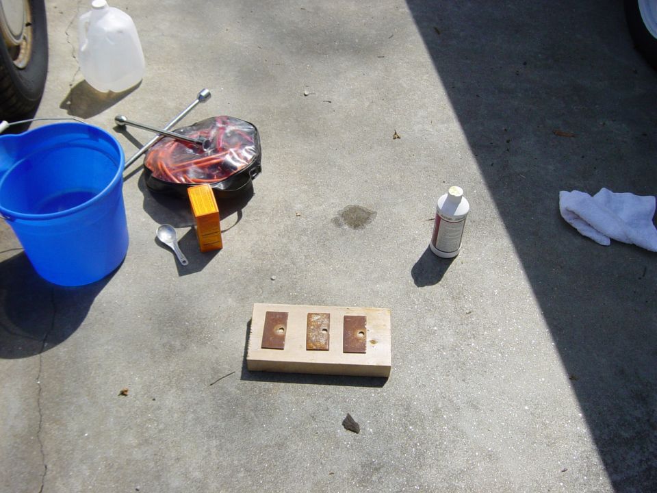 blue bucket, water jug, jack, and a wooden block with metal plates on concrete