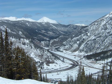 1992 Ford Probe - A vast, snow-covered mountain valley is bisected by a highway, with trees dotting the slopes under a clear blue sky.