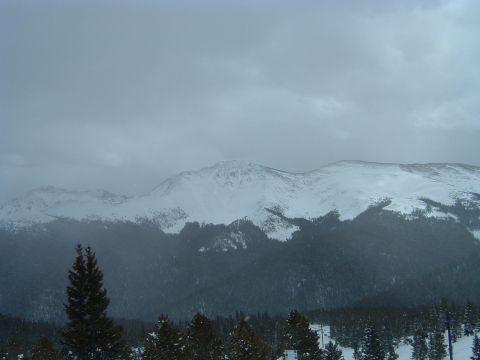 1992 Ford Probe - A vast, snow-covered mountain range stretches across the horizon under a cloudy sky, with dark evergreen trees dotting the foreground.