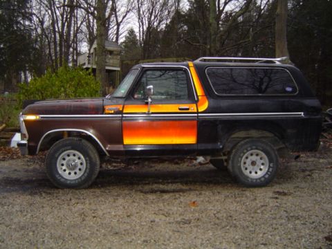 1979 Ford Bronco - Driver-side profile of a black full-size two-door Ford Bronco with an orange and yellow sunburst bodyside stripe and a removable hardtop, p…