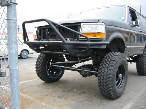 1992 Ford Bronco - Low front three-quarter shot of a lifted black Ford Bronco in a parking lot, with the grille and front fascia removed to expose a black tub…