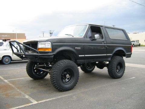 1992 Ford Bronco - Front three-quarter view of a lifted black full-size Ford Bronco with a removable hardtop, black tube front bumper, BRONCO fender badge, an…