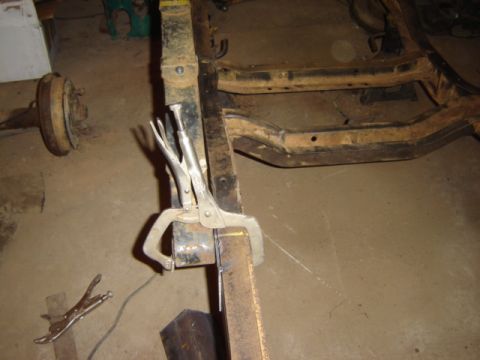 1992 Ford Bronco - Close-up of a vehicle frame being worked on, with tools attached and a rear axle in the background.