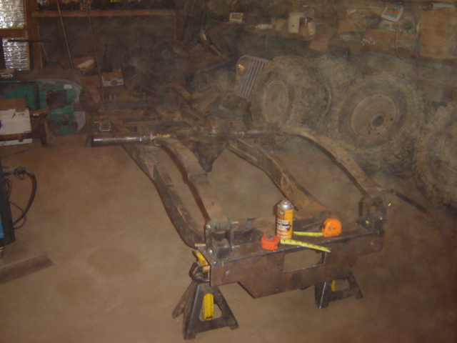 Vehicle frame on jack stands in a garage, with tools and tires in the background