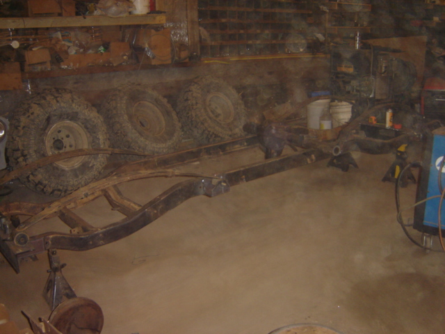 Vehicle frame and four tires stacked in a workshop