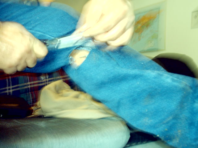 Person cutting a hole in blue jeans with scissors. Supermotors.net logo visible