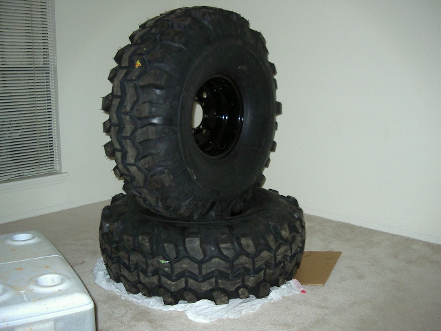 Two large off-road tires stacked indoors. One tire is on top of the other