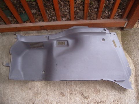 1993 Ford Probe - A gray molded plastic interior trim panel, likely a trunk or cargo-area side liner, laid face-up on a concrete patio in front of a red-stai…