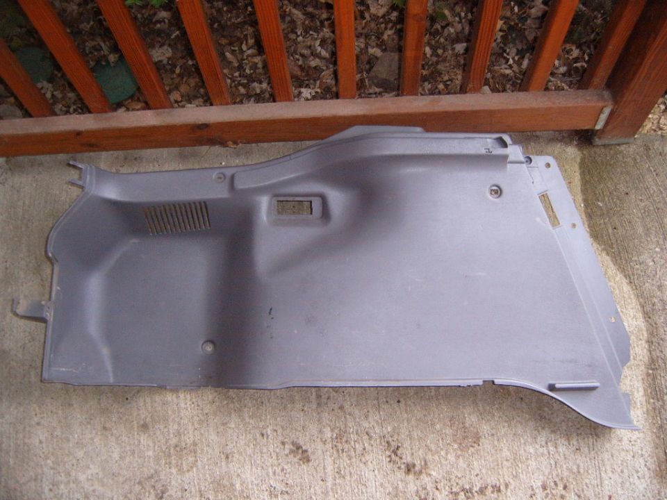 Gray plastic trunk side trim panel with vent slots lying on concrete by a wood railing