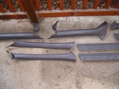 1993 Ford Probe - A set of gray plastic interior pillar and sill trim pieces spread across a concrete slab in front of a stained wood deck railing, including…
