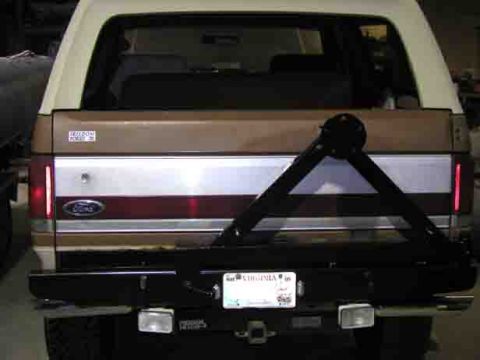 1988 Ford Bronco - Rear view of a two-tone tan and white full-size Ford Bronco fitted with a black steel rear bumper and a swing-out tire carrier arm, with ba…
