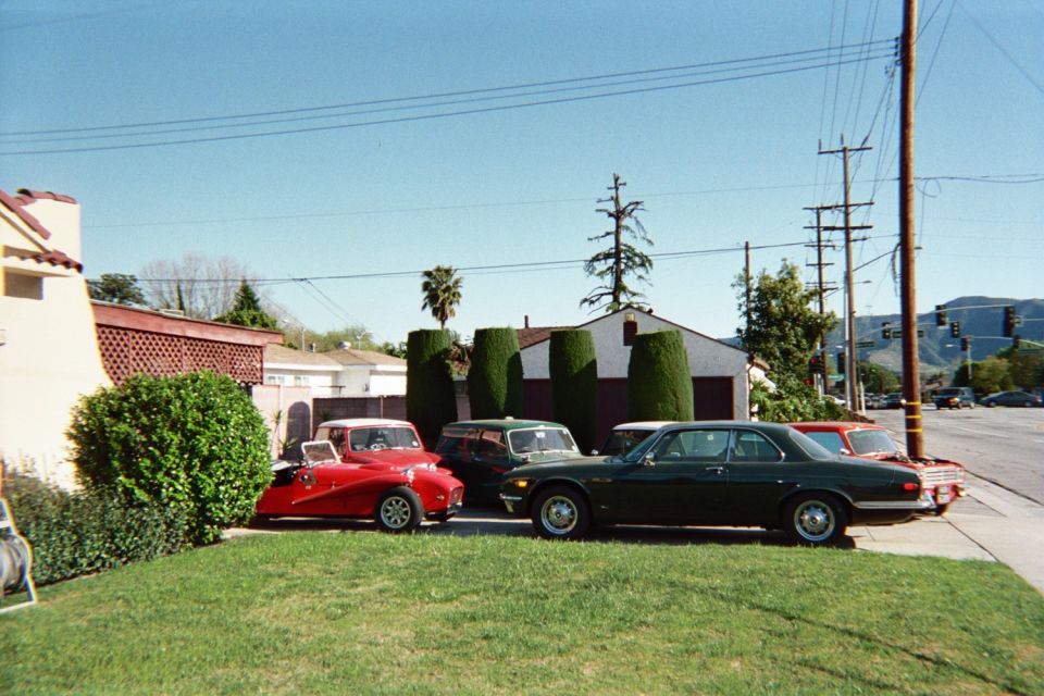 Red roadster, dark green coupe and red sedan parked on a grass lawn beside a residential driveway