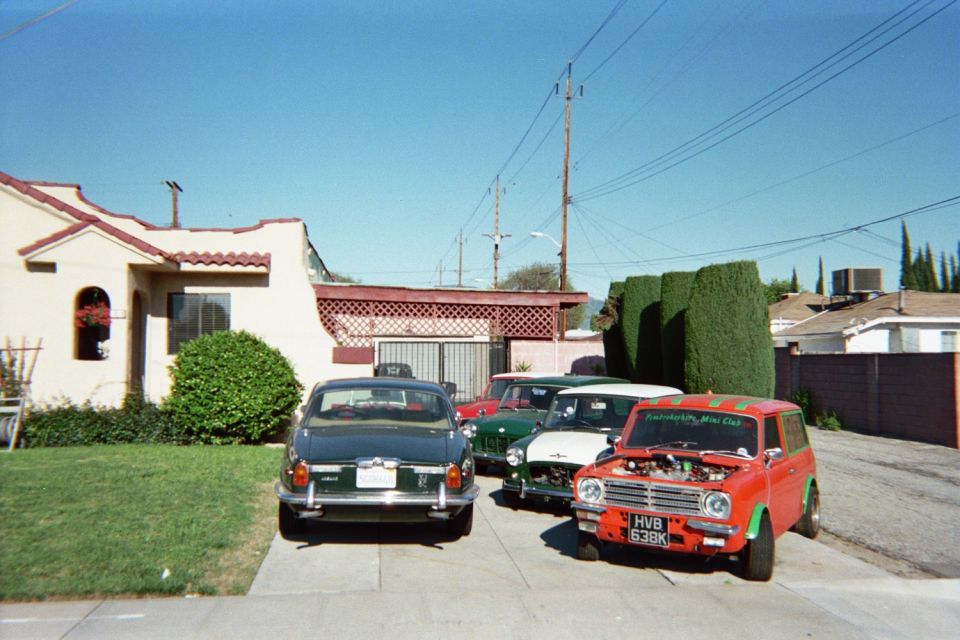 Row of classic British-style cars including a red Mini parked in a driveway by a stucco house